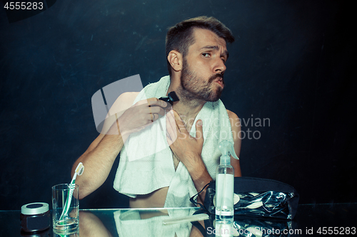 Image of The young man in bedroom sitting in front of the mirror scratching his beard