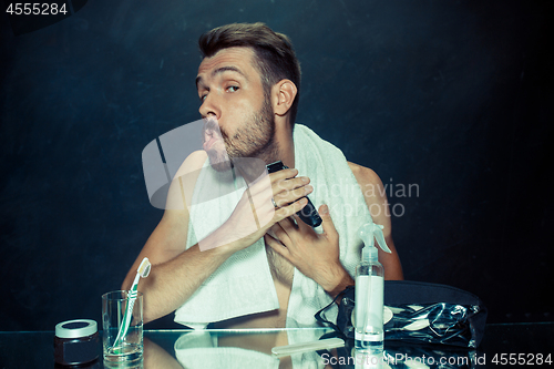 Image of The young man in bedroom sitting in front of the mirror scratching his beard