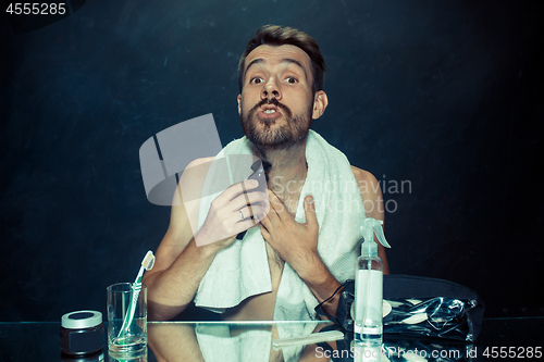 Image of The young man in bedroom sitting in front of the mirror scratching his beard