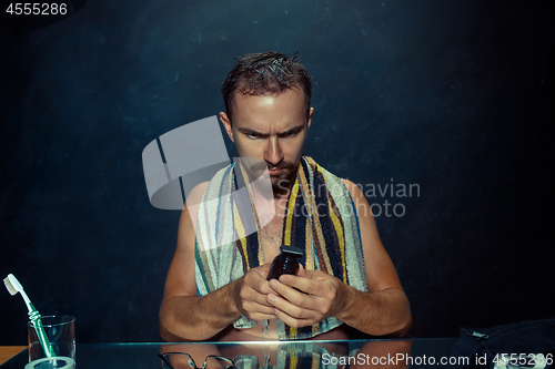 Image of The young man in bedroom sitting in front of the mirror scratching his beard