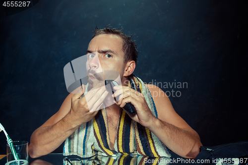 Image of The young man in bedroom sitting in front of the mirror scratching his beard