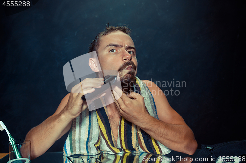 Image of The young man in bedroom sitting in front of the mirror scratching his beard