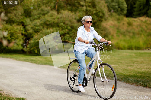 Image of happy senior woman riding bicycle at summer park