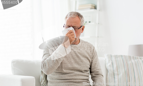 Image of sick senior man with paper wipe blowing his nose