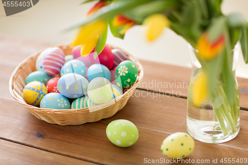 Image of colored easter eggs in basket and flowers at home