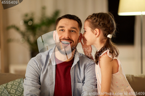 Image of happy daughter whispering secret to father at home