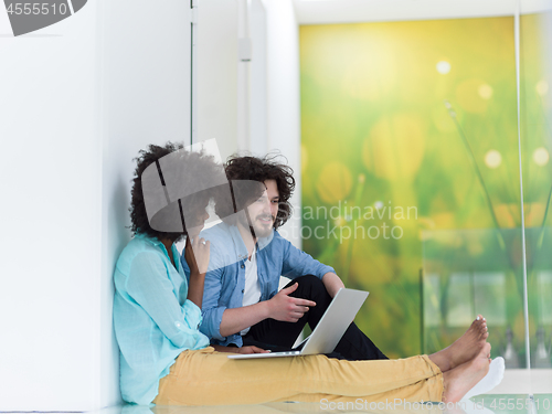 Image of multiethnic couple using a laptop on the floor