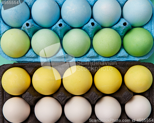 Image of A collection of painted yellow, green, white and blue eggs in cardboard boxes. Creative Easter background. Flat lay