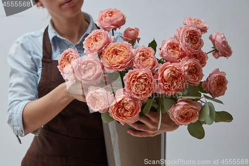 Image of Female hands holding a vase with flowers of pink roses around a gray background. The concept of a flower shop