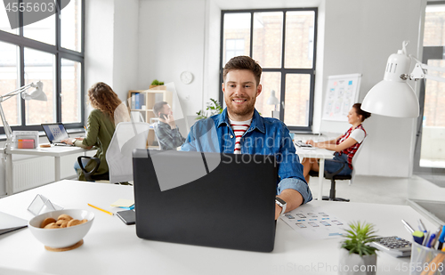 Image of smiling creative man with laptop working at office