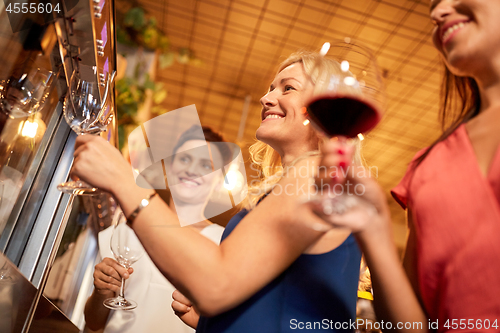 Image of happy women pouring wine from dispenser at bar