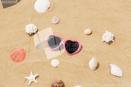 Image of heart-shaped sunglasses and shells on beach sand