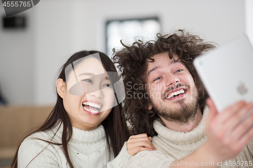 Image of multiethnic couple using tablet computer in front of fireplace