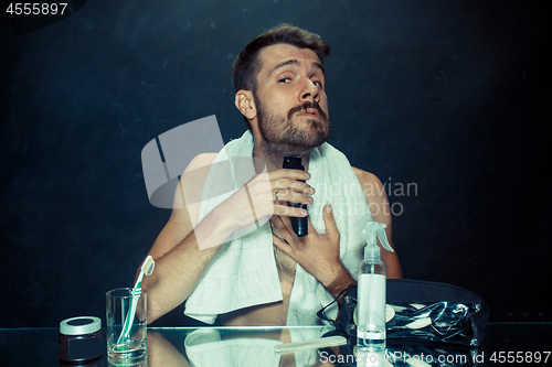 Image of The young man in bedroom sitting in front of the mirror scratching his beard