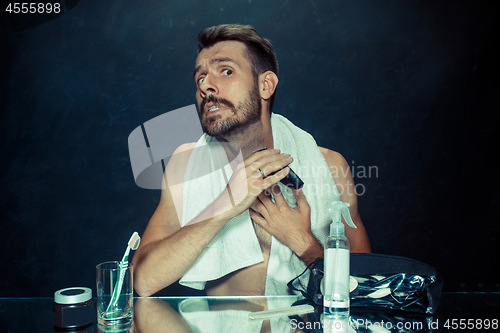 Image of The young man in bedroom sitting in front of the mirror scratching his beard