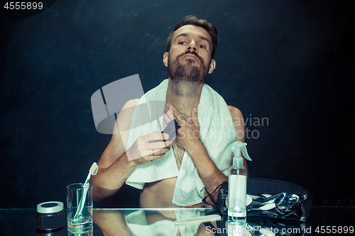 Image of The young man in bedroom sitting in front of the mirror scratching his beard