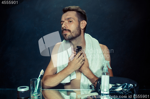 Image of The young man in bedroom sitting in front of the mirror scratching his beard