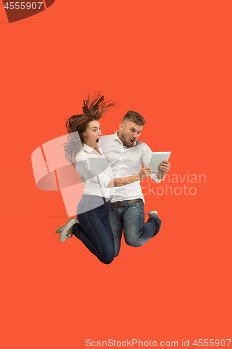 Image of Image of young couple over red background using laptop computer or tablet gadget while jumping.