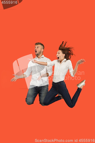 Image of Freedom in moving. Surprised young couple jumping against red background