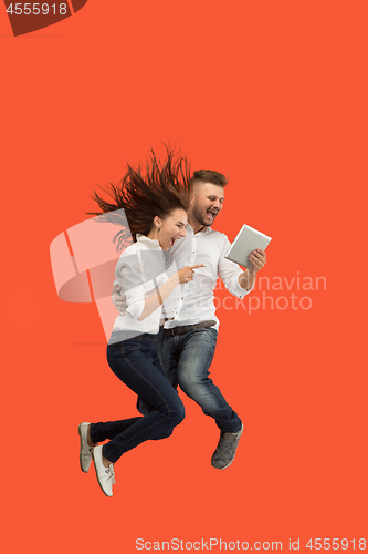 Image of Image of young couple over red background using laptop computer or tablet gadget while jumping.