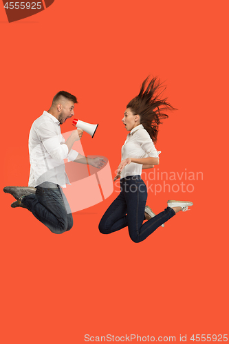 Image of Beautiful young couple jumping with megaphone isolated over red background