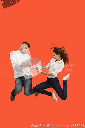 Image of Beautiful young couple jumping with megaphone isolated over red background