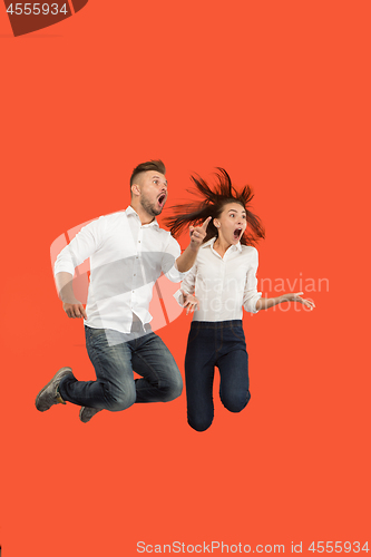 Image of Freedom in moving. Surprised young couple jumping against red background