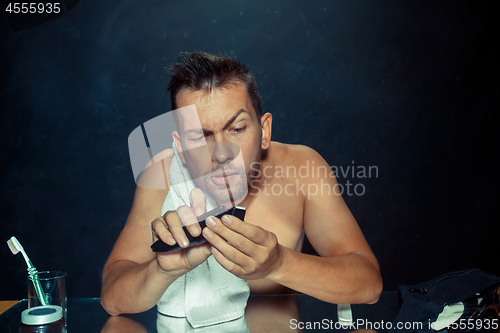 Image of The young man in bedroom sitting in front of the mirror scratching his beard