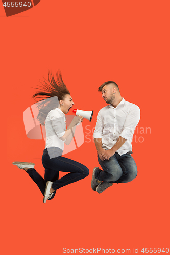 Image of Beautiful young couple jumping with megaphone isolated over red background