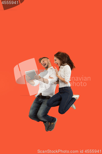 Image of Image of young couple over red background using laptop computer or tablet gadget while jumping.