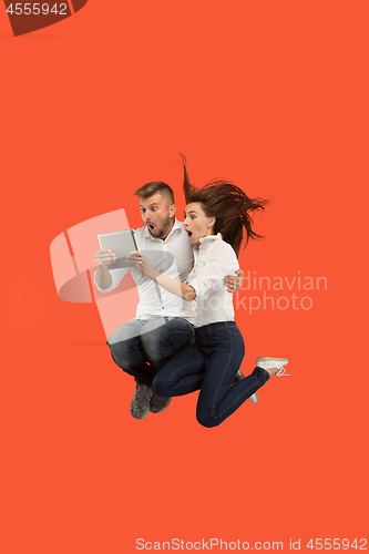 Image of Image of young couple over red background using laptop computer or tablet gadget while jumping.