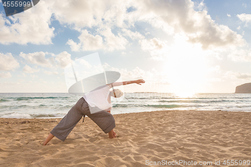 Image of Woman practicing yoga on sea beach at sunset.