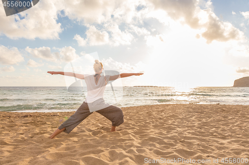 Image of Woman practicing yoga on sea beach at sunset.