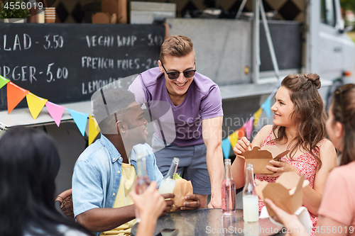 Image of happy friends with drinks eating at food truck