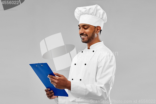 Image of happy male indian chef in toque with clipboard