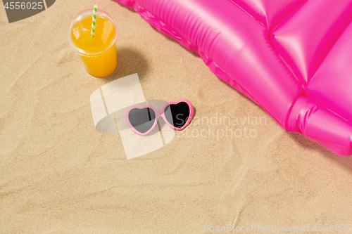 Image of sunglasses, juice and pool mattress on beach sand