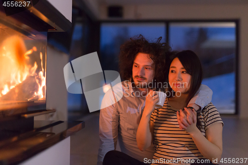 Image of happy multiethnic couple sitting in front of fireplace