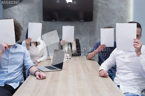 Image of startup business team holding a white paper over face