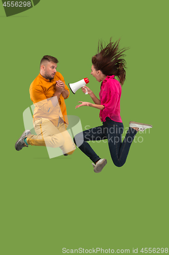 Image of Beautiful young couple jumping with megaphone isolated over green background