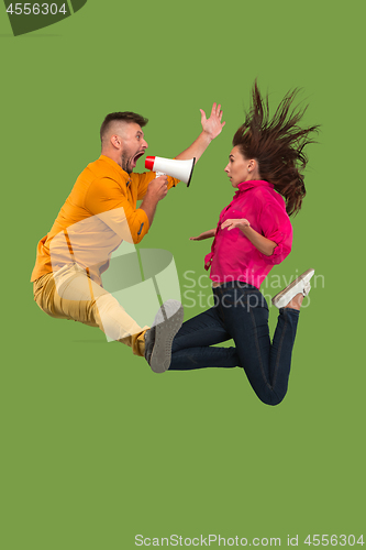 Image of Beautiful young couple jumping with megaphone isolated over green background