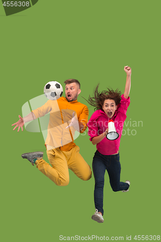 Image of Forward to the victory.The young couple as soccer football player jumping and kicking the ball at studio on a green