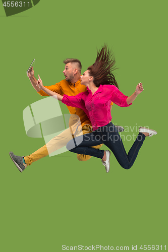 Image of Jump of young couple over green studio background using laptop or tablet gadget while jumping.