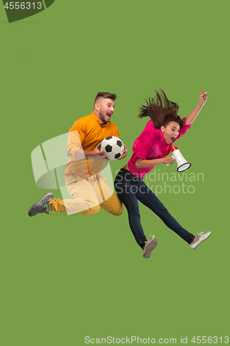 Image of Forward to the victory.The young couple as soccer football player jumping and kicking the ball at studio on a green