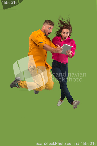 Image of Jump of young couple over green studio background using laptop or tablet gadget while jumping.