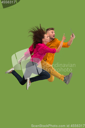 Image of Jump of young couple over green studio background using laptop or tablet gadget while jumping.