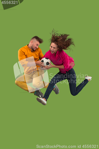 Image of Forward to the victory.The young couple as soccer football player jumping and kicking the ball at studio on a green