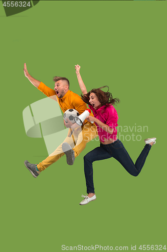 Image of Forward to the victory.The young couple as soccer football player jumping and kicking the ball at studio on a green