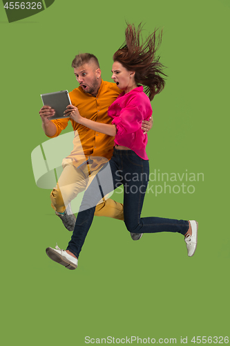 Image of Jump of young couple over green studio background using laptop or tablet gadget while jumping.