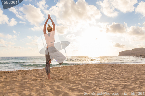 Image of Woman practicing yoga on sea beach at sunset.