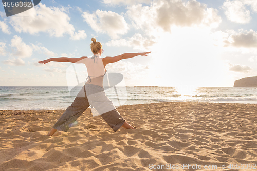 Image of Woman practicing yoga on sea beach at sunset.